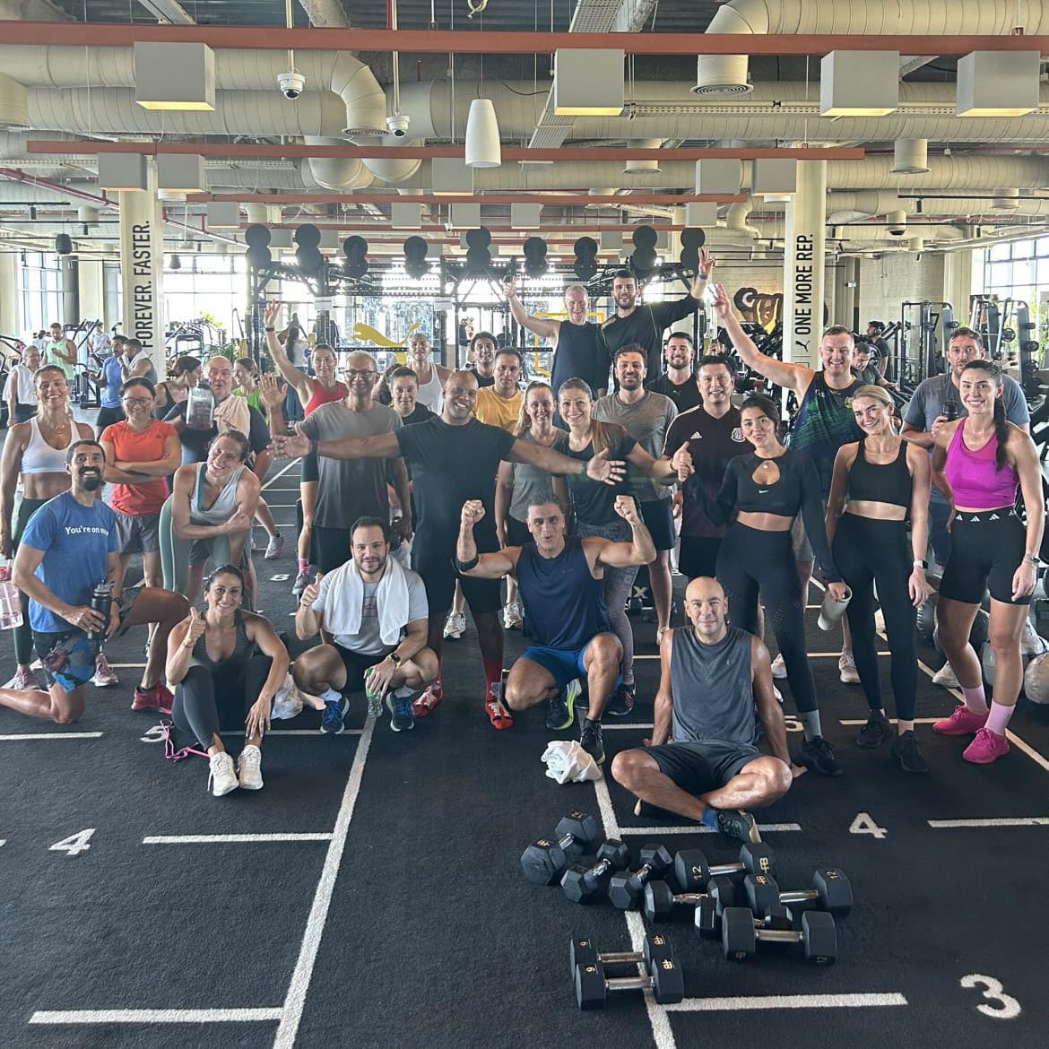 A large group of diverse people smiling and posing for a commemorative photo inside a bright, modern CrossFit gym.